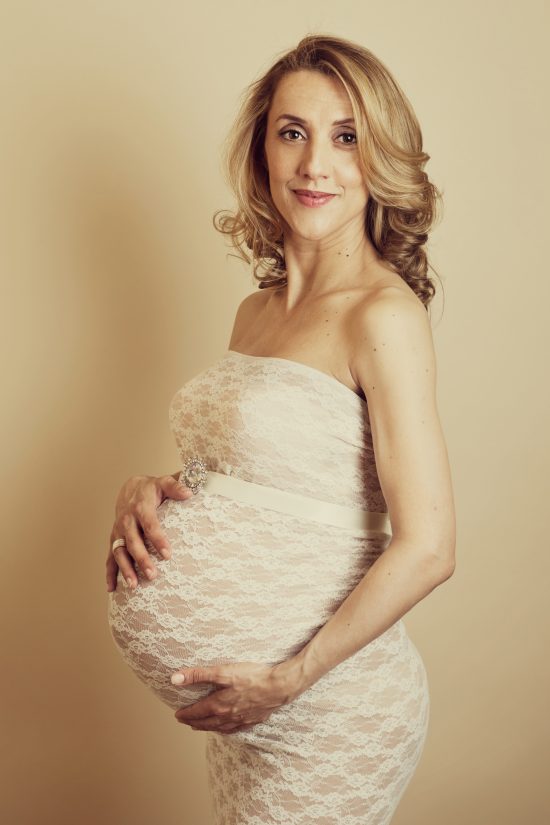 stunning-pregnant-woman-in-a-lace-fitted-dress-holding-her-bump-maternity-photography-surrey