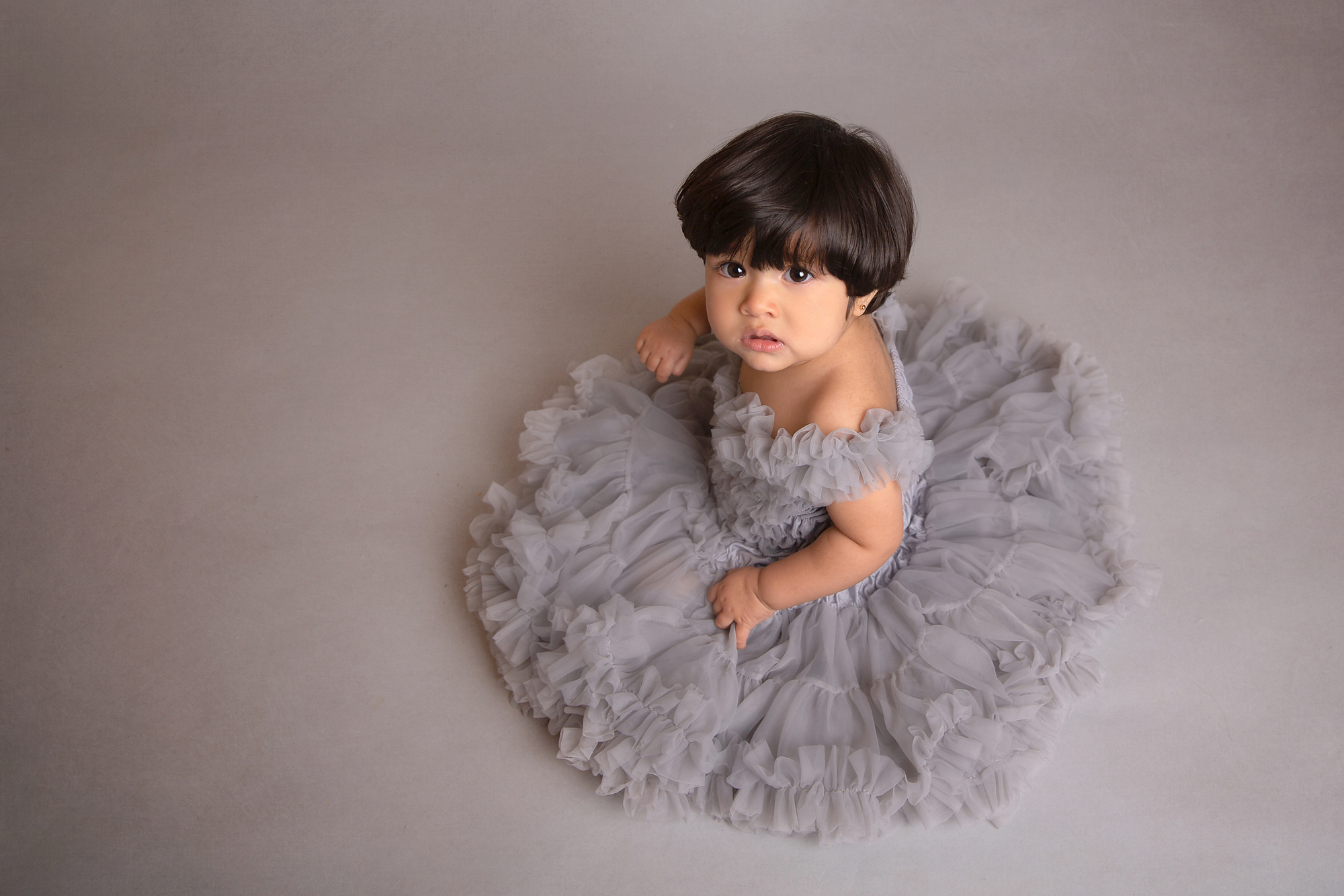 baby-girl-in-grey-frilly-dress-looking -up-by-surrey-baby-photographer