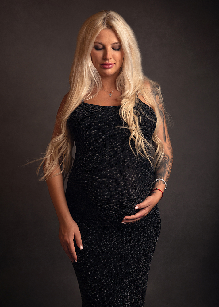 pregnant woman in black sparkly dress looking lovingly at bump by Surrey Maternity Photographer